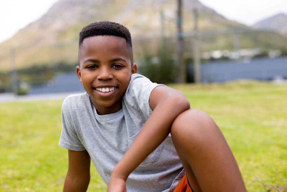 child therapist in eastbourne, A boy smiling, looking relaxed sitting on the grass.